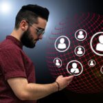 man met baard en bril kijkt op zijn smartphone. Op de achtergrond zien we een soort van wereldbol met symbolen die zijn contacten voorstellen.