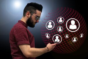 man met baard en bril kijkt op zijn smartphone. Op de achtergrond zien we een soort van wereldbol met symbolen die zijn contacten voorstellen.