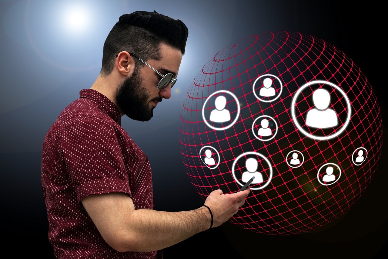 man met baard en bril kijkt op zijn smartphone. Op de achtergrond zien we een soort van wereldbol met symbolen die zijn contacten voorstellen.
