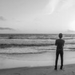 Jongeman kijkt vanaf het strand naar de horizon.