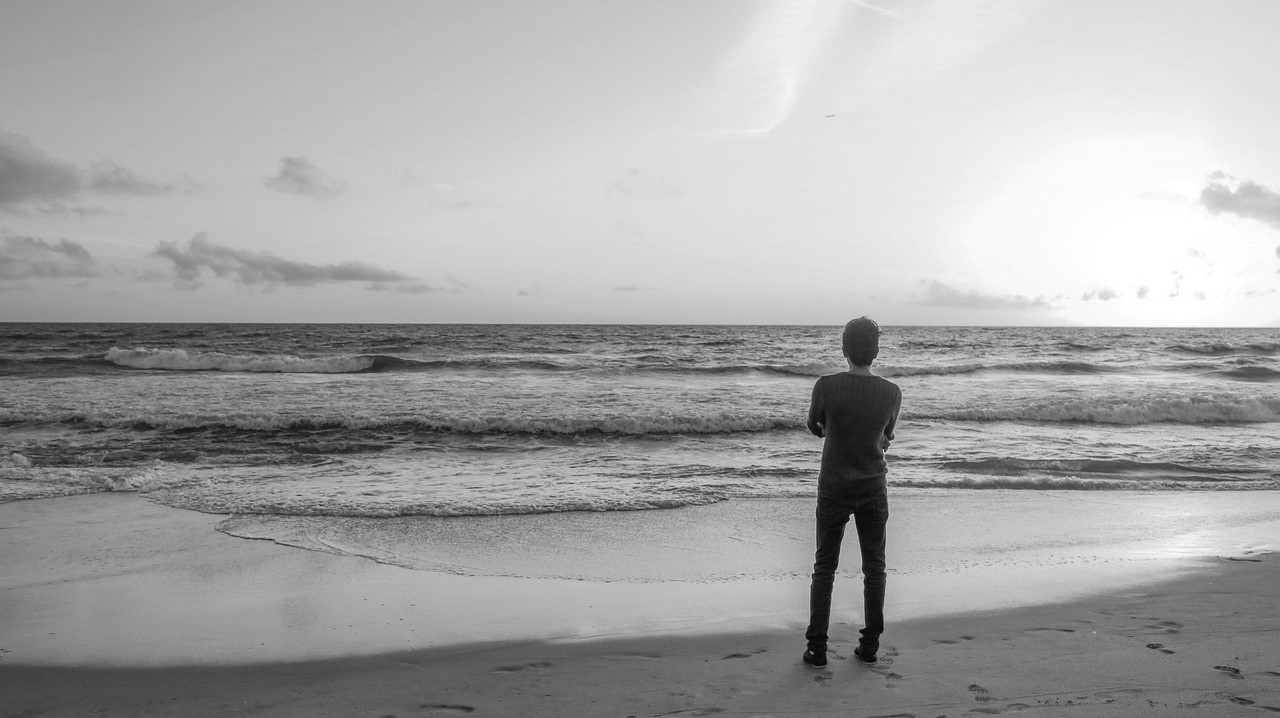 Jongeman kijkt vanaf het strand naar de horizon.